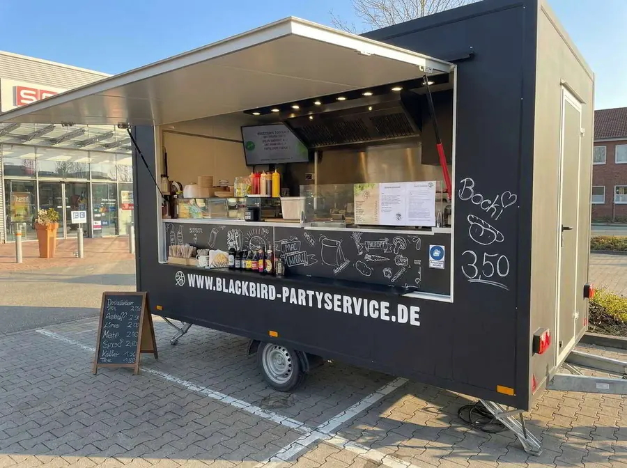 Der schwarze Blackbird Foodtruck mit aufgeklappter Klappe und Chalkboard-Menü.